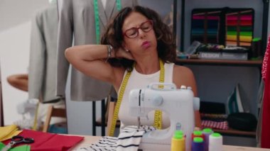 Middle age woman tailor stressed using sewing machine at clothing factory