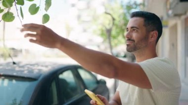 Young hispanic man smiling confident making photo to tree sheet at street