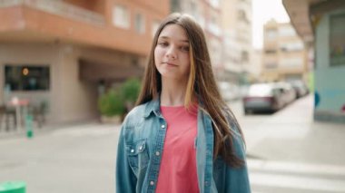 Sevimli kız gülümsüyor. Kendine güveni tam. Sokakta elleriyle fotoğraf hareketi yapıyor.