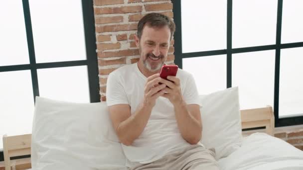 Middelbare Leeftijd Man Met Behulp Van Smartphone Zitten Bed Slaapkamer — Stockvideo