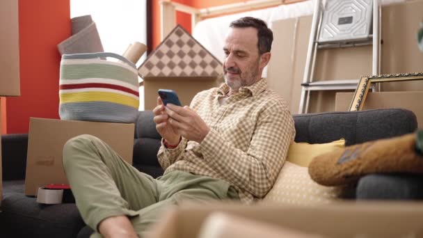 Orta Yaşlı Bir Adam Yeni Evindeki Koltukta Akıllı Telefon Kullanıyor — Stok video