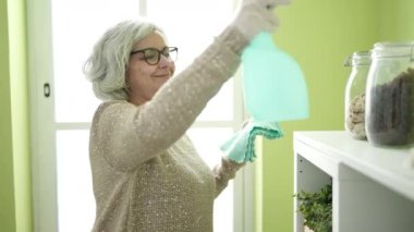 Beyaz saçlı, orta yaşlı bir kadın evinde temizlik yapıyor.