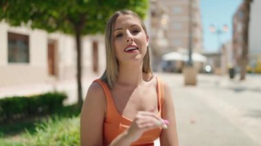 Genç, güzel, İspanyol bir kadın, gülümsüyor. Parktaki bankta oturuyor.