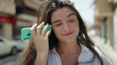 Young hispanic woman smiling confident listening audio message by the smartphone at street