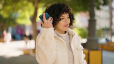 Young hispanic woman smiling confident listening audio message by the smartphone at park