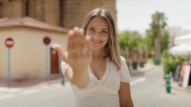 Genç beyaz kadın gülümsüyor. Kendinden emin. Sokakta el kol hareketi yapıyor.