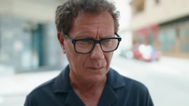 Orta yaşlı, rahat yüzlü bir adam sokakta dikiliyor.