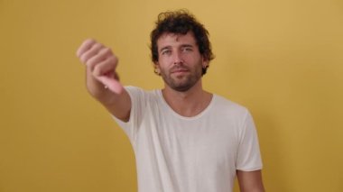 Genç İspanyol adam, izole edilmiş sarı arka plan üzerinde olumsuz jest yapıyor.