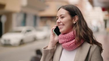 Gülümseyen genç bir kadın caddedeki akıllı telefondan konuşuyor.