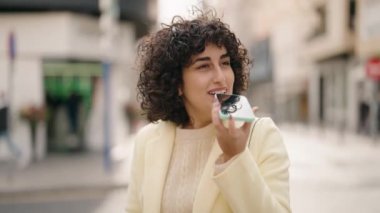 Gülümseyen genç bir kadın caddedeki akıllı telefondan konuşuyor.