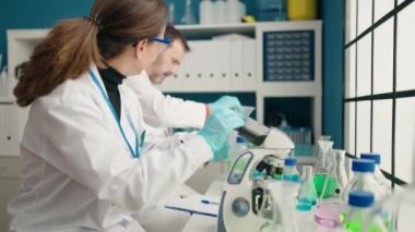 Man and woman scientists using microscope working at laboratory