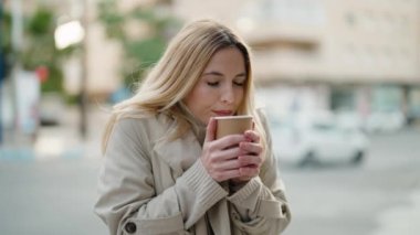 Young blonde woman smiling confident drinking coffee at street