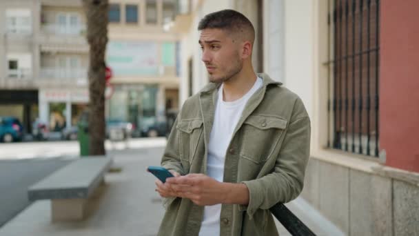Jonge Spaanse Man Glimlacht Vol Vertrouwen Met Behulp Van Smartphone — Stockvideo