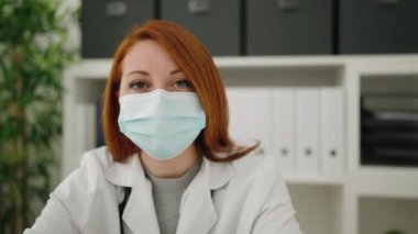 Young redhead woman wearing doctor uniform and medical mask working at clinic