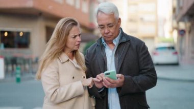 Caddede akıllı telefon kullanan neşeli yüzlü orta yaşlı çift.