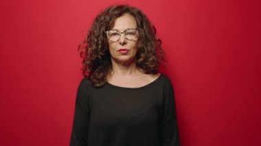 Orta yaşlı bir kadın kırmızı arka planda kurabiye tutarken kendine güler.