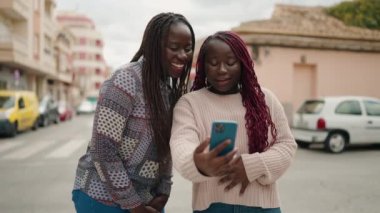 Two african american women smiling confident having video call at street