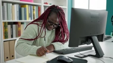 Örgülü saçlı Afrikalı kadın üniversite kütüphanesinde sırt ağrısı olan bir bilgisayar kullanıyor.