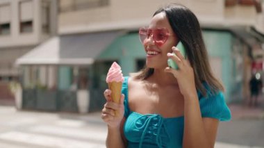 Genç İspanyol kadın akıllı telefondan konuşuyor. Sokakta dondurma yiyor.