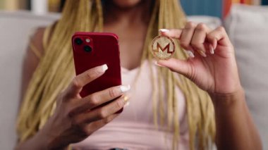 Evde akıllı telefon kullanarak Monero kripto para birimini elinde tutan Afrikalı Amerikalı kadın.