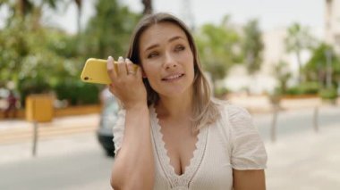 Beyaz kadın gülümsüyor. Caddedeki akıllı telefondan kendine güvenen sesli mesaj dinliyor.