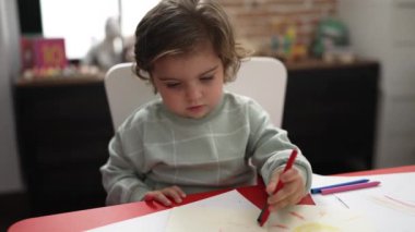 Anaokulunda masaya oturmuş kağıda resim çizen sevimli İspanyol kız öğrenci.
