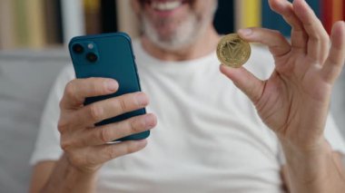 Evde akıllı telefon kullanan orta yaşlı bir adam tron kripto para birimini tutuyor.