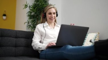Young blonde woman having video call sitting on sofa at home