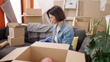 Genç beyaz kadın yeni evinde karton kutu paketliyor.