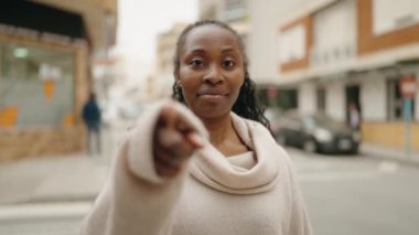 Afro-Amerikalı kadın gülümsüyor. Kendinden emin. Sokakta el kol hareketi yapıyor.