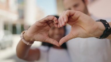 Man and woman interracial couple doing heart gesture with hands at street