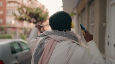 Genç Afrikalı Amerikalı kadın gülümsüyor. Kendine güveniyor. Müzik dinliyor ve sokakta dans ediyor.