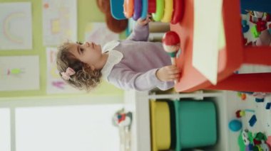 Adorable hispanic girl playing maraca standing at kindergarten