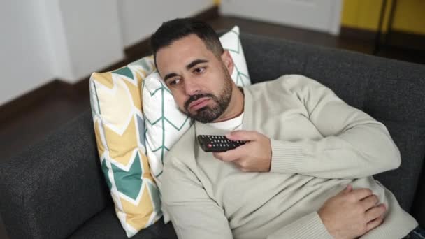 Junger Hispanischer Mann Sieht Fernsehen Auf Sofa Liegend Mit Langweiligem — Stockvideo