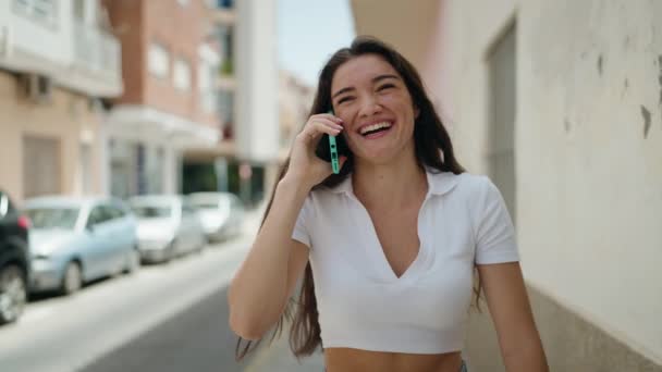 若いヒスパニック系の女性が自信を持ってスマートフォンで話して笑顔通りを歩く — ストック動画