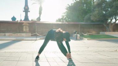 Orta yaşlı kadın spor giyiniyor. Gülümsüyor. Sokakta esniyor.