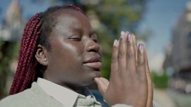 Saçları örgülü Afrikalı kadın parkta gözleri kapalı dua ediyor.