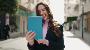 Sokakta dokunmatik ped kullanan genç İspanyol kadın gülümsüyor.