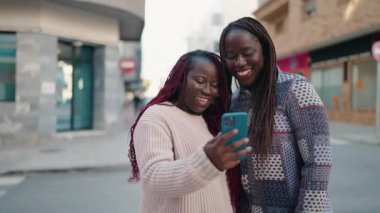 Two african american women smiling confident using smartphone at street