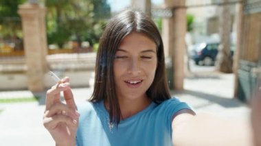 Genç, güzel İspanyol kadın sokakta sigara içerken görüntülü arama yapıyor.