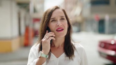 Genç, güzel, İspanyol bir kadın gülümsüyor ve caddede akıllı telefondan konuşuyor.