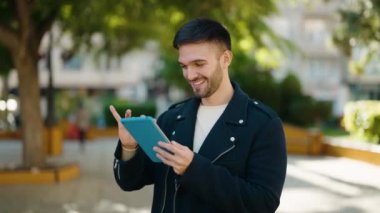 Young hispanic man smiling confident using touchpad at park
