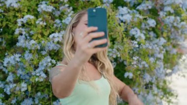 Parktaki akıllı telefonun yanında kendinden emin gülümseyen genç sarışın kadın.