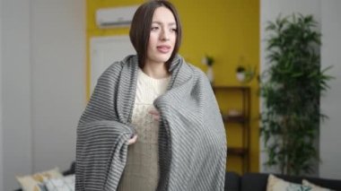 Young beautiful hispanic woman covering with blanket for cold at home