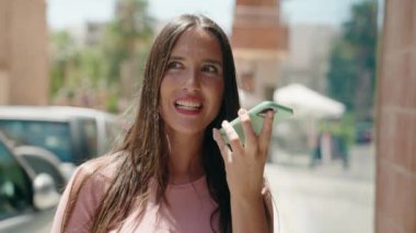 Genç, güzel, İspanyol bir kadın gülümsüyor ve caddede akıllı telefondan konuşuyor.