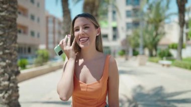 Young beautiful hispanic woman miling confident listening audio message by the smartphone at park