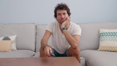Young hispanic man watching movie sitting on sofa at home