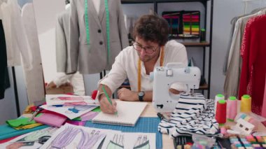 Young hispanic man tailor drawing on notebook at clothing factory