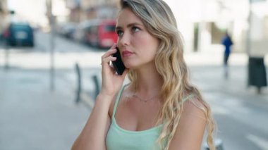 Sokakta endişeli bir ifadeyle akıllı telefondan konuşan genç sarışın kadın.