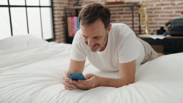 使用智能手机的中年人躺在卧室的床上 — 图库视频影像